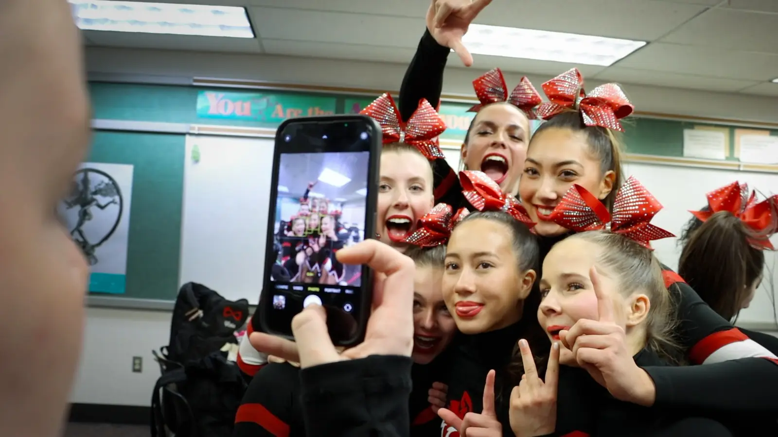 Still from documentary, cheerleaders in red bows crowd together for a group selfie