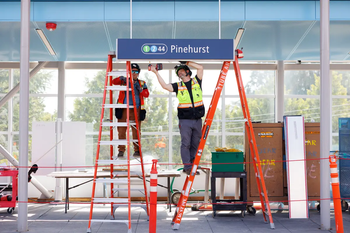 Two workers on ladders install a Pinehurst station sign