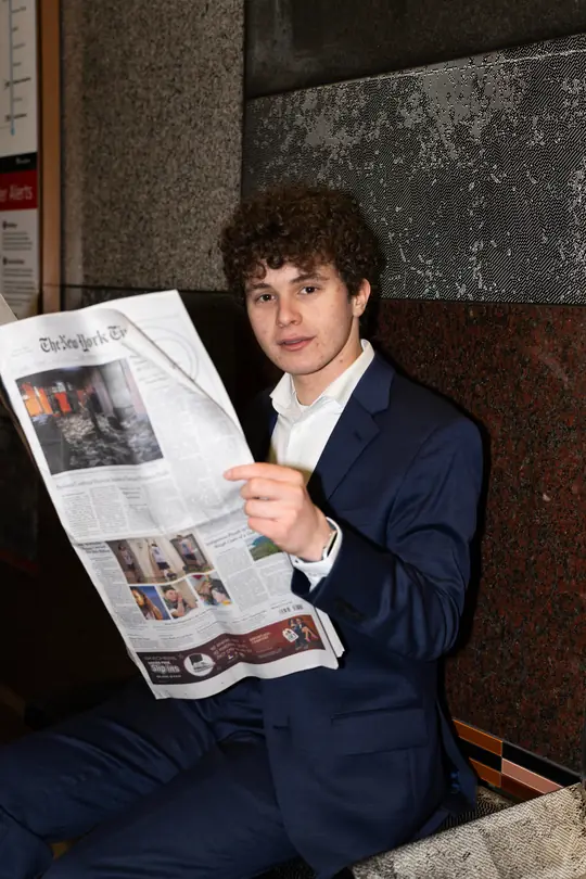 Jonah Kessler-Cohen, in a navy suit, looks up from reading a newspaper